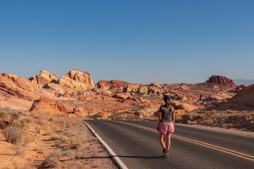 Woman standing on endless winding empty road in Valley of Fire State Park leading to red Aztec...