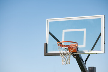 Clear glass basketball backboard with rim on blue sky background with copy space