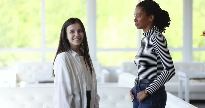 Joyful happy pretty diverse female friends meeting in cafe with greeting hug, smiling, laughing, saying hello, talking, chatting. Positive young multiethnic women enjoying friendship