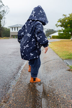 Toddler girl wearing raincoat splashing in gutter at roadside