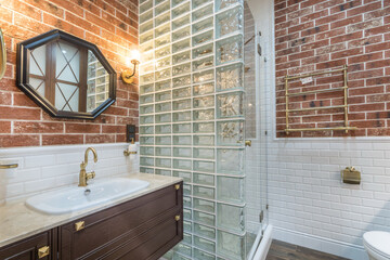 Stylish design of the bathroom, decorated with brick tiles. The wall of the shower cabin .is made of glass blocks.
