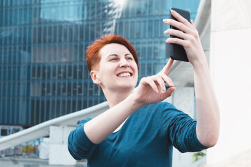 Woman with short red hair takes a selfie on the smartphone. Blogger broadcasts. Communication on the phone, social networks