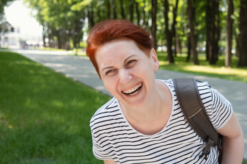 Portrait of a middle-aged woman with short red hair in a striped t-shirt. Woman looks away and laughs. Walk in the city park.