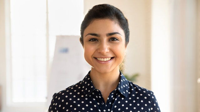 Close up headshot portrait of smiling young indian female employee look at camera posing in office, profile picture of millennial ethnic woman worker show confidence optimism at workplace