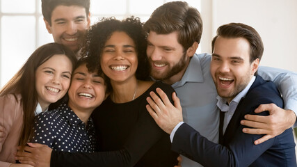 Overjoyed diverse multiracial colleagues have fun cuddle embrace celebrating shared business...
