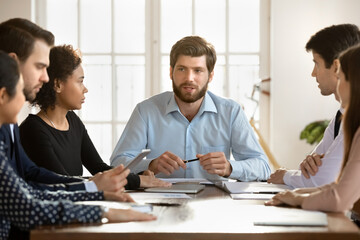 Confident Caucasian businessman lead meeting with multiracial colleagues in office, diverse businesspeople talk brainstorm discuss business ideas together at briefing, collaboration concept