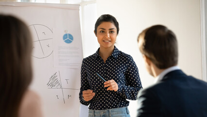 Confident young indian female coach or speaker talk make flip chart presentation for employees at meeting, focused ethnic businesswoman or leader present business project on whiteboard at briefing - Powered by Adobe