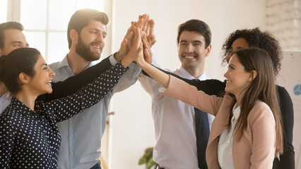 Excited multiracial employees give high five engaged in teambuilding activity in office together,...