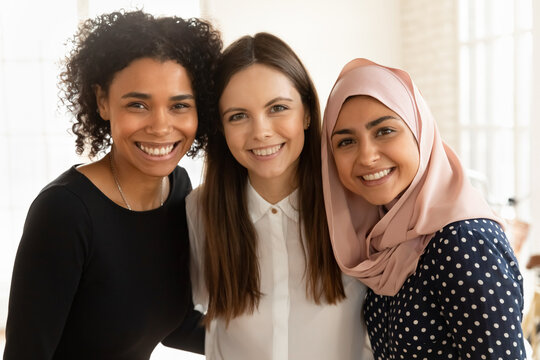 Portrait of smiling multiethnic female employees colleagues hug embrace pose together in international office, happy diverse multiracial women interns students show unity and friendship in relations
