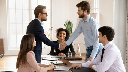 Smiling businessman stand at meeting shake hands get acquainted greeting in office, happy male business partners handshake close deal make agreement at briefing, acquaintance, partnership concept