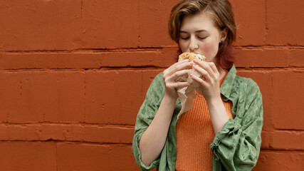 Street food concept. Caucasian young woman eating burger outside. Banner, copy space.