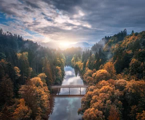  Aerial view of wooden bridge over the river in mountains at foggy autumn morning in Slovenia. Top drone view of bridge, orange forest, hills, fog, cloudy sky at sunrise in fall. Nature. Road in woods © den-belitsky