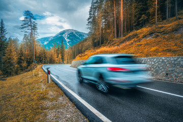 Blurred car in motion on the road in orange forest in rain in autumn. Dolomites, Italy. Perfect...