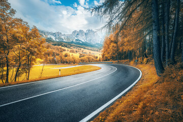 Road in mountains at sunny day in golden autumn. Dolomites, Italy. Beautiful roadway, orange tress, high rocks, blue sky with clouds. Landscape with empty highway through the mountain pass in fall - obrazy, fototapety, plakaty