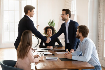Smiling male colleagues employees shake hands get acquainted greeting at office team meeting,...