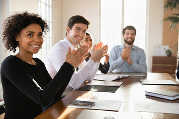 Smiling diverse employees sit at desk applaud greeting trainer or speaker at meeting in office, overjoyed multiethnic colleagues clap hands thanking coach for briefing, acknowledgement concept