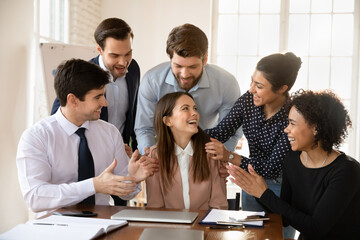 Happy multiracial employees applaud greeting excited young Caucasian female colleague with good...
