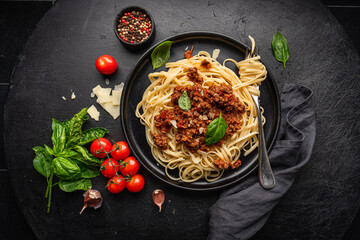 Pasta spaghetti bolognese with minced beef sauce, tomatoes, parmesan cheese and fresh basil in a plate on black tile background. Italian food, top view