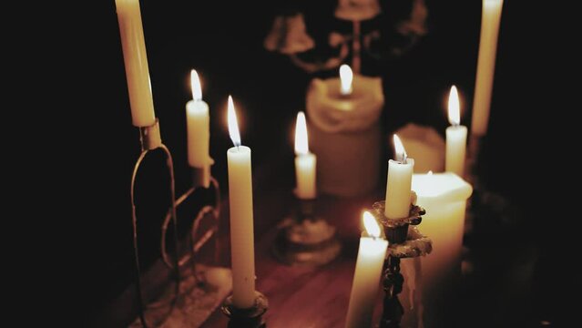 Many burning candles on the wooden table in dark room, light only from candles, burning candles on the piano, slow motion shot.