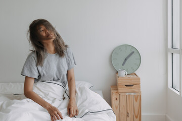 Asian woman just wake up by the clock at 7 AM on the bed in the morning.