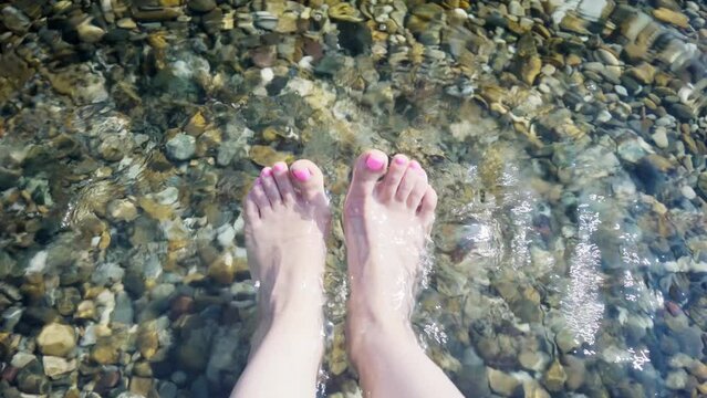 close-up of a women's feet threading in cold water, making a splash, on a hot, sunny day