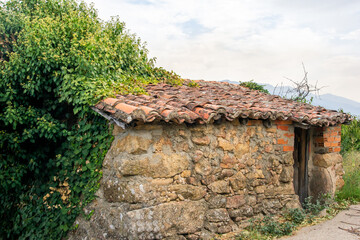 Antigua caseta de aperos agr&iacute;colas, construida con rocas, con un viejo tejado, y parcialmente cubierta por plantas enredaderas.