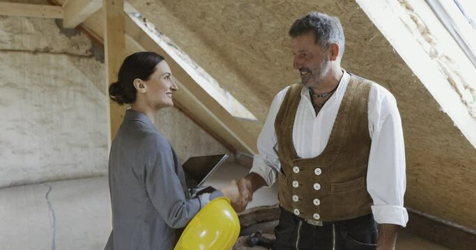female and carpenter on construction site interior looking howing blueprints of the project, shaking hands