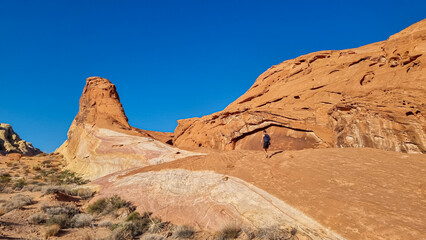 Fototapeta premium Man climbing striated red and white rock formations along the White Domes Hiking Trail in Valley of Fire State Park in Mojave desert, Nevada, USA, America. Unique natural landmark shaped like a spire