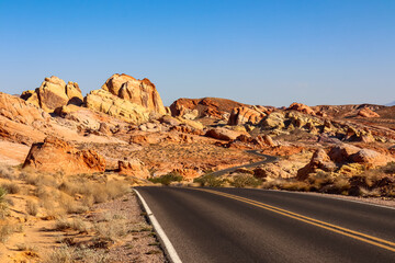 Panoramic view of endless winding empty road in Valley of Fire State Park leading to red Aztec Sandstone Rock formations and desert vegetation in Mojave desert, Overton, Nevada, USA. Freedom road trip
