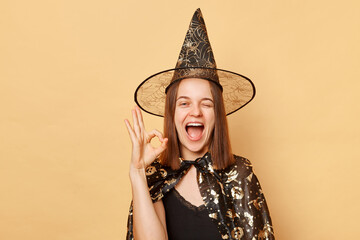 Smiling young woman wearing witch costume and carnival cone hat celebrating halloween isolated over...
