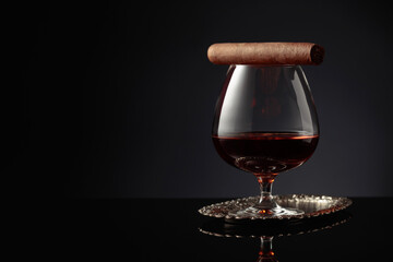 Snifter of brandy and cigar on a black background.