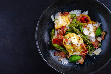 Green glazed asparagus with fried prosciutto ham, croxetti pasta and parmesan cheese served as top view on a design plate with text space left