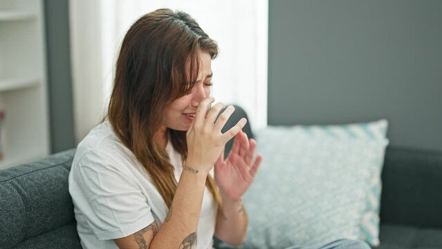 Young beautiful hispanic woman sitting on the sofa crying at home