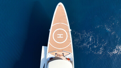 Aerial drone photo of mega yacht with wooden deck and helicopter landing area anchored in deep blue...