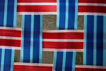 Vibrant blue and red webbing of a vintage lawn chair. Playful pattern, pop of color. Retro design, summer vibes. Perfect for outdoor seating, vintage decor. Eye-catching detail, timeless appeal.