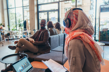 Muslim female employee talking to her black male colleague at work while reading sales reports at the office