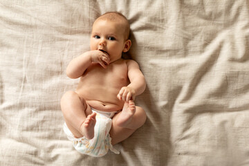 Glad little baby in diaper lying on soft bed, waking after sleep in bedroom, copy space, top view. Family, parenthood care, kid newborn at home