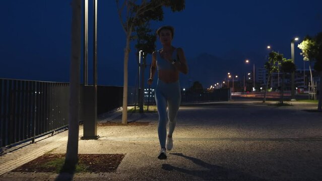 Beautiful Busty Fitness Girl in Blue Athletic Top and Jogging on the Street. She is Doing a Workout in a Night. High quality 4k footage