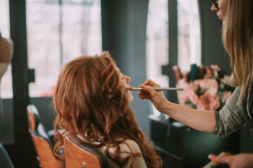 Fototapeta premium Professional hairstylist putting face powder to a ginger client.
