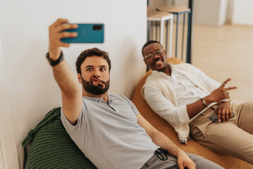 Two colleagues making faces and taking a selfie during break at work