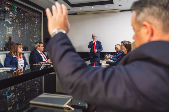 Senior Businessman Raising Hand To Ask Question During Meeting At The Office.