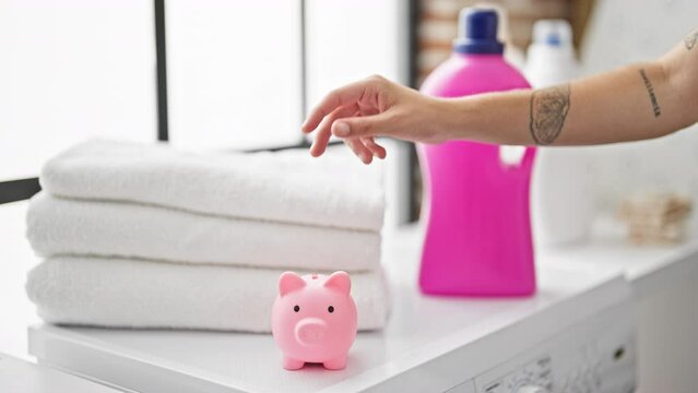 Young beautiful hispanic woman inserting coin on piggy bank at laundry room