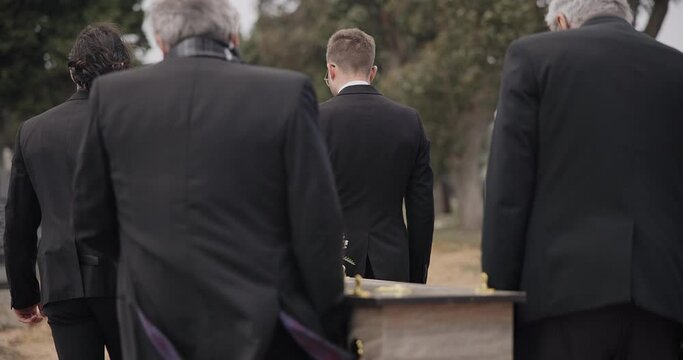 Men, coffin and pallbearers walking at funeral ceremony outdoor for burial together. Death, grief and group carry casket at cemetery, graveyard and family service of people mourning at windy event