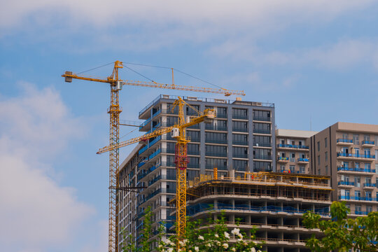 Two yellow tower cranes and unfinished building construction against the blue sky with clouds in Batumi. Urban, industrial, engineering and developing concept