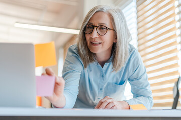 Portrait of smiling confident senior woman wearing stylish eyeglasses using laptop planning...