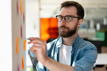 Pensive bearded man, successful scrum master  using sticky notes, agile methodology for...