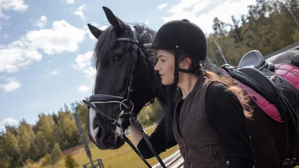 Foto op Canvas Equestrian sports. A young woman, a rider and her horse, going out for training near the stable © Ulia Koltyrina