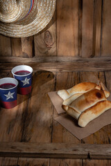 Fototapeta na wymiar Chilean independence day concept. fiestas patrias. Tipical baked empanadas de pino, wine or chicha, hat and play emboque. Dish and drink on 18 September party, wooden background