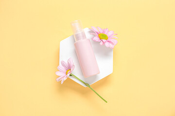Plaster podium with bottle of cosmetic product and beautiful flowers on color background
