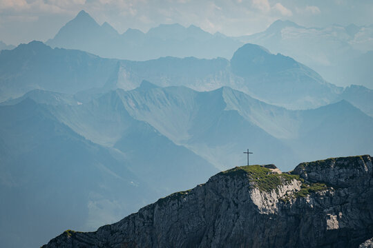 Alpine panorama featuring a cross and layered mountain peaks on a blue horizon 
